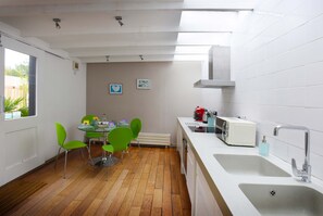 A modern kitchen with a dining area, featuring a wooden floor, white tiles, and green chairs.