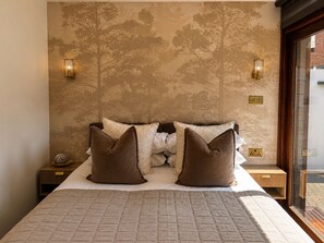 A bedroom with a large bed, two nightstands, a wall-mounted lamp, and a window with a view.