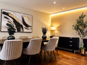 A modern dining area with a long table, six chairs, a large abstract painting, a floor lamp, and a potted plant. - Cedar House at The Old Fire Station (Canterbury)