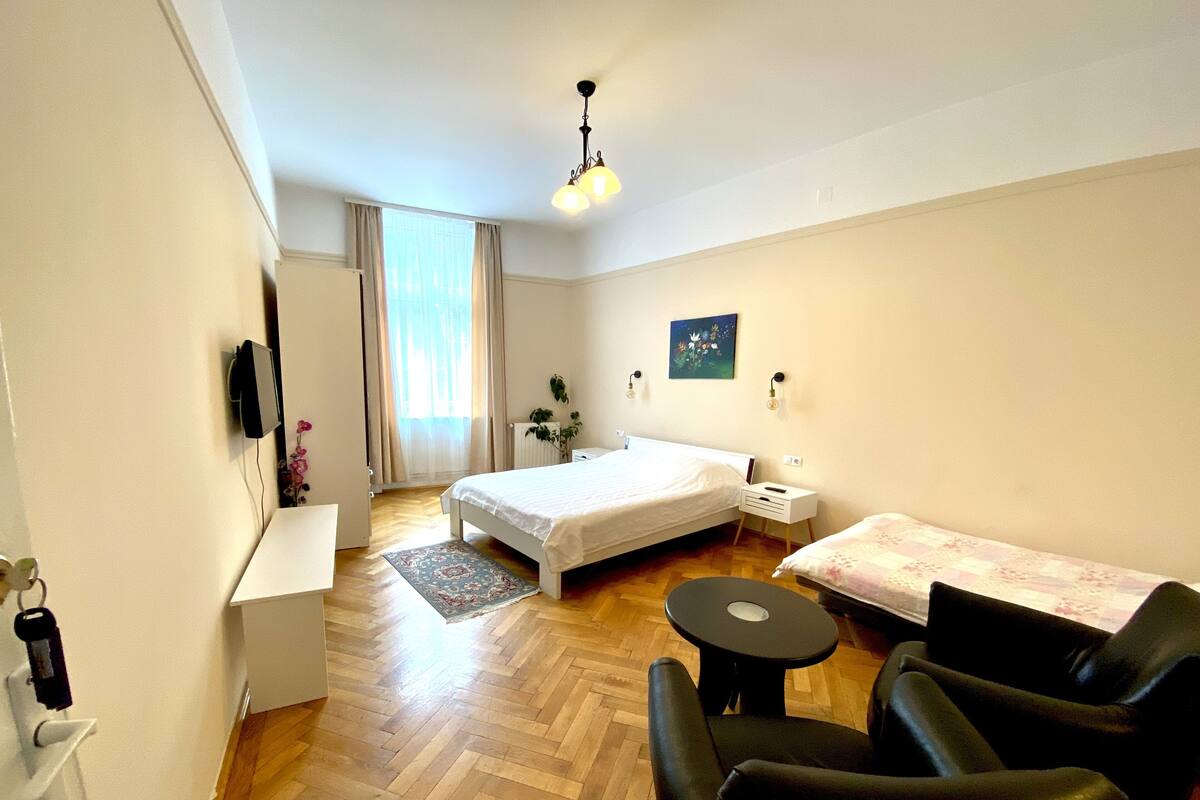 A hotel room with a bed, a desk, a chair, a small table, and a window with curtains.