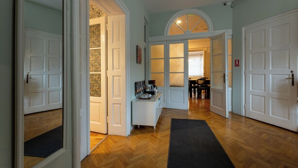 A hallway with wooden flooring, white doors, a black rug, and a desk with a chair. - Casa Balcescu (Brasov)