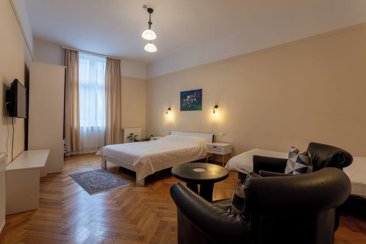 A hotel room with a bed, a desk, a chair, a small table, and a TV.