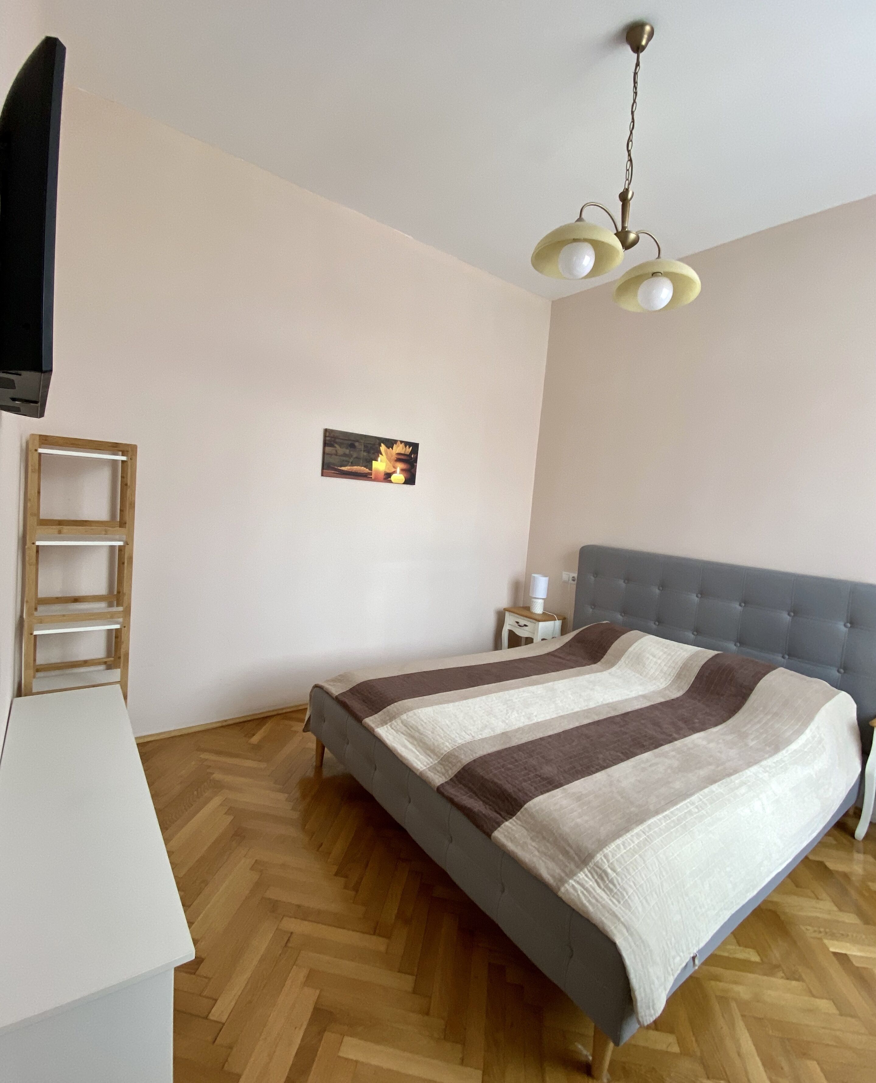 Un dormitorio con una cama, televisión, mesita de noche, lámpara y un cuadro en la pared.