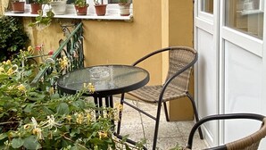 A patio with a round table and two wicker chairs, surrounded by potted plants and a window with multiple panes. - Casa Balcescu (Brasov)