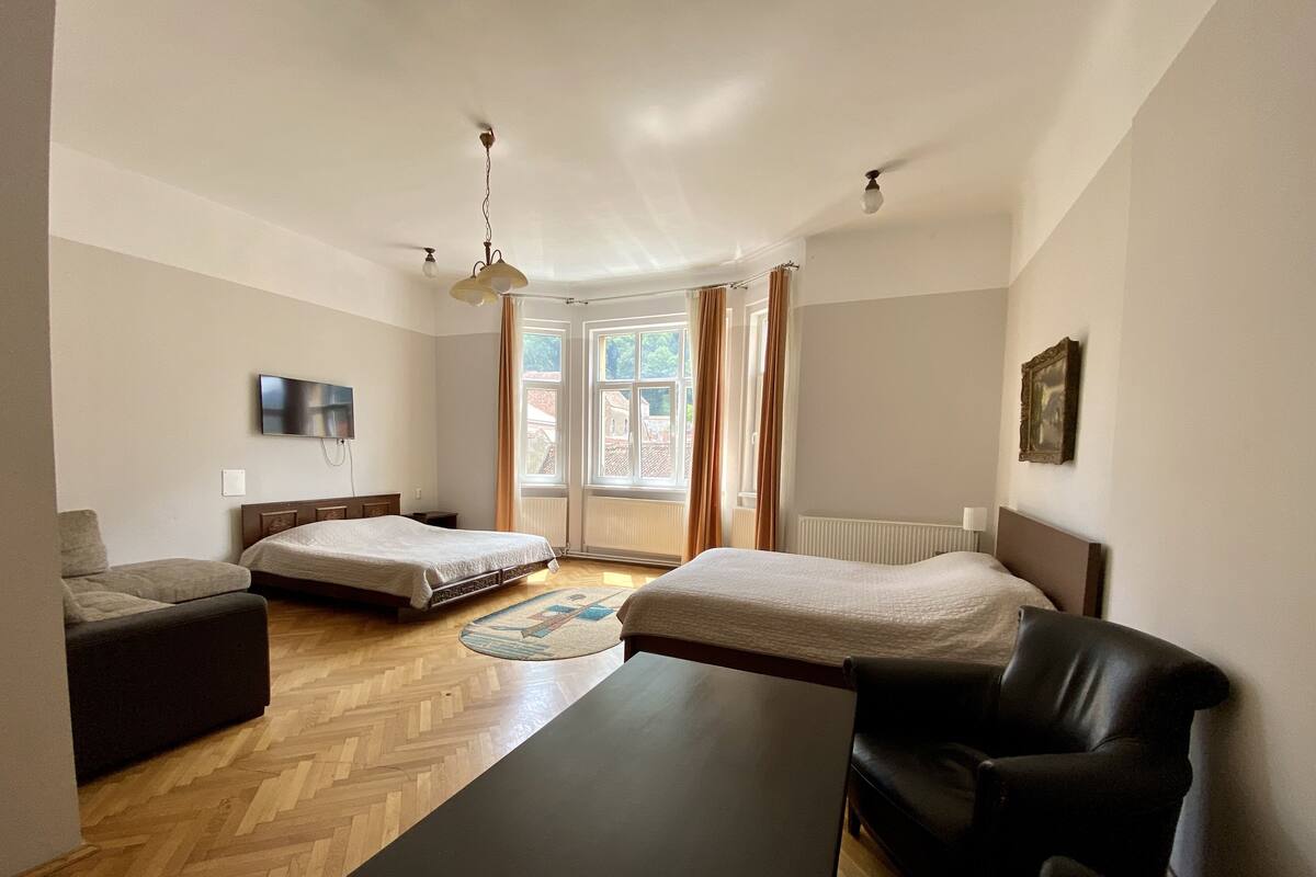 A modern hotel room with two beds, a sofa, a table, and a TV.