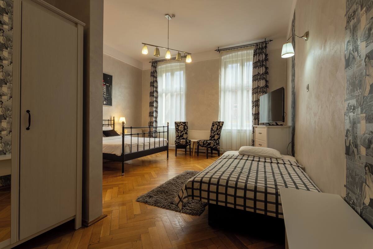 A bedroom with a bed, two chairs, a desk, a TV, and a wardrobe.