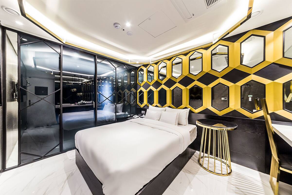 Una habitación de hotel moderna con una cama grande, un panel de vidrio y un diseño geométrico en la pared.