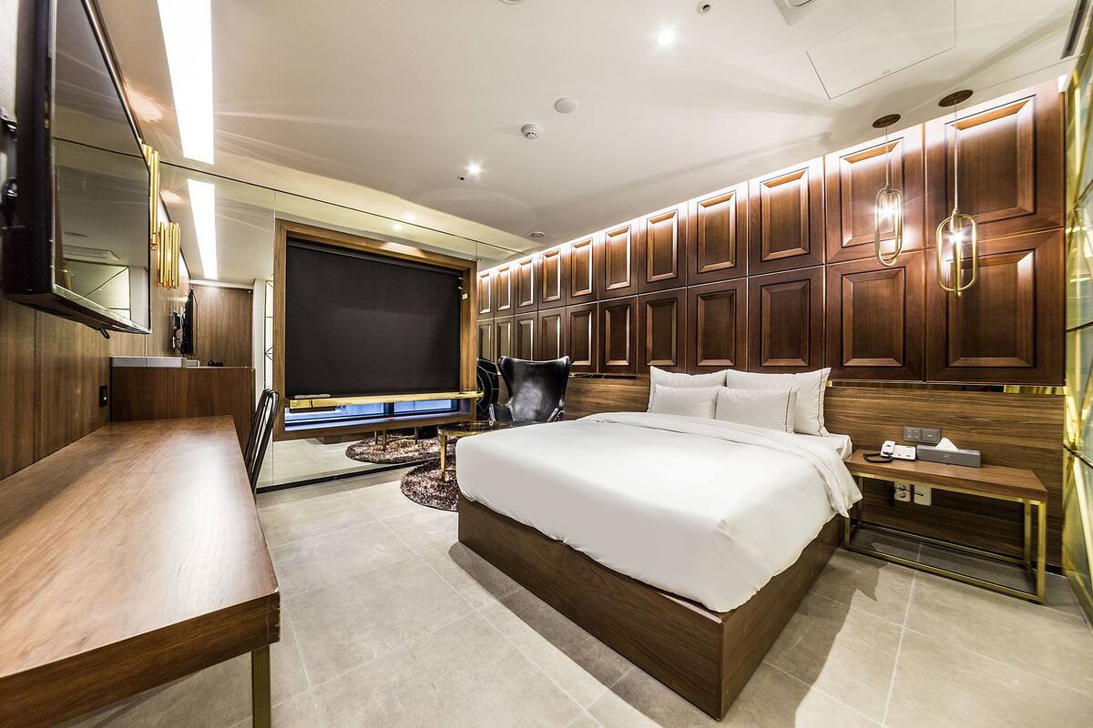 Una habitación de hotel moderna con una cama grande, un televisor de pantalla plana, paneles de madera y un escritorio de madera.