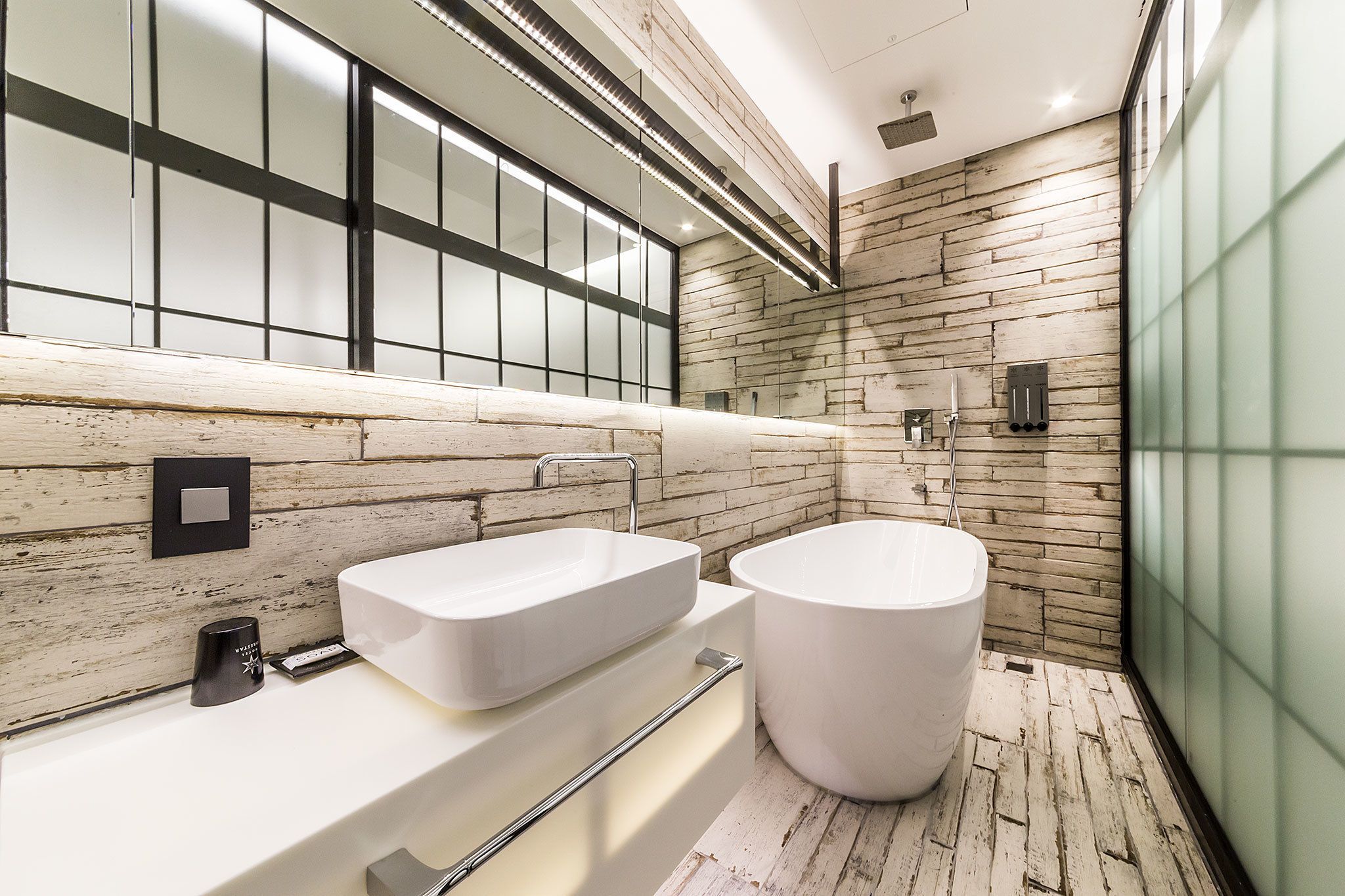 Un baño moderno con un lavabo rectangular grande y una bañera independiente, paneles de pared de madera y una mampara de vidrio.