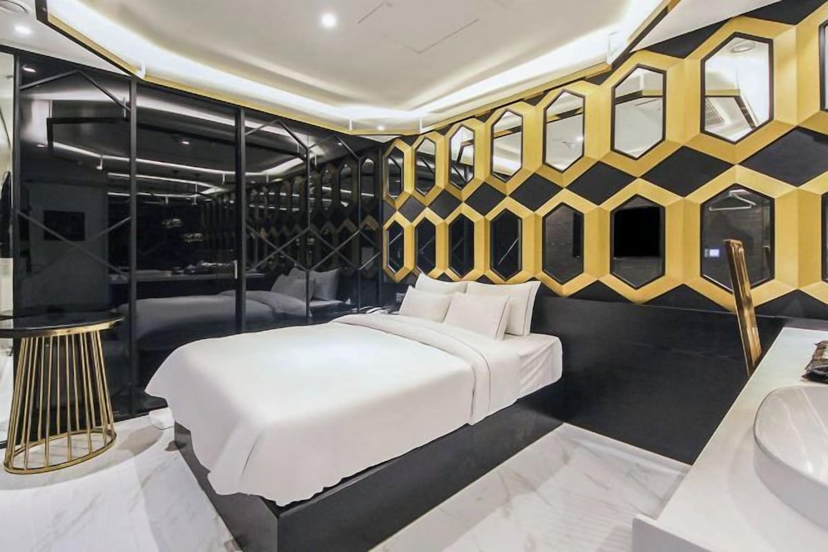 A modern bedroom with a bed, a black and gold geometric wall design, and a glass partition.