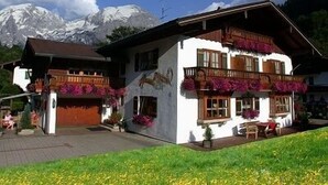 Ein traditionelles Chalet mit Holzbalkonen, einem Bergpanorama und einer gepflasterten Auffahrt.