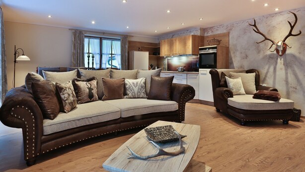 Ein modernes Wohnzimmer mit einem braunen Ledersofa, einem Holztisch und einem Essbereich mit Holzschränken sowie einer Küche im Hintergrund.