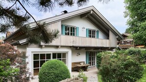 Una casa de dos pisos con un balcón, un banco de madera y una planta en maceta.