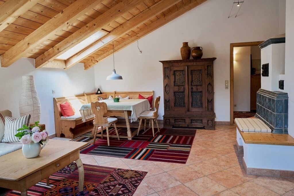 A cozy room with a wooden ceiling, a dining area with a table and chairs, a cabinet, and a bench.