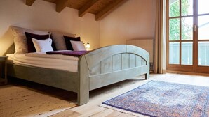 Un dormitorio con cama, mesita de noche, ventana con cortinas y techo de madera.