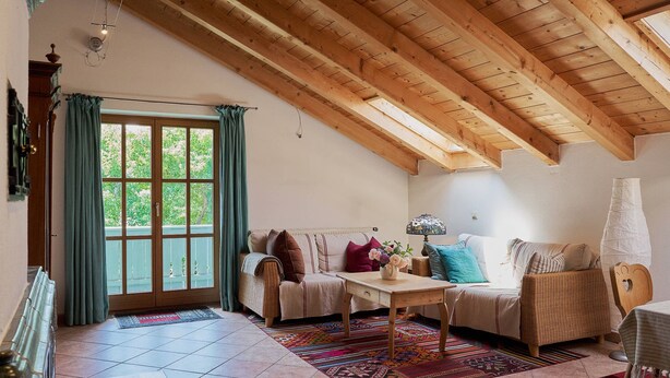 Una sala de estar acogedora con un alto techo de madera, un sofá, una mesa y vistas por un gran ventanal.