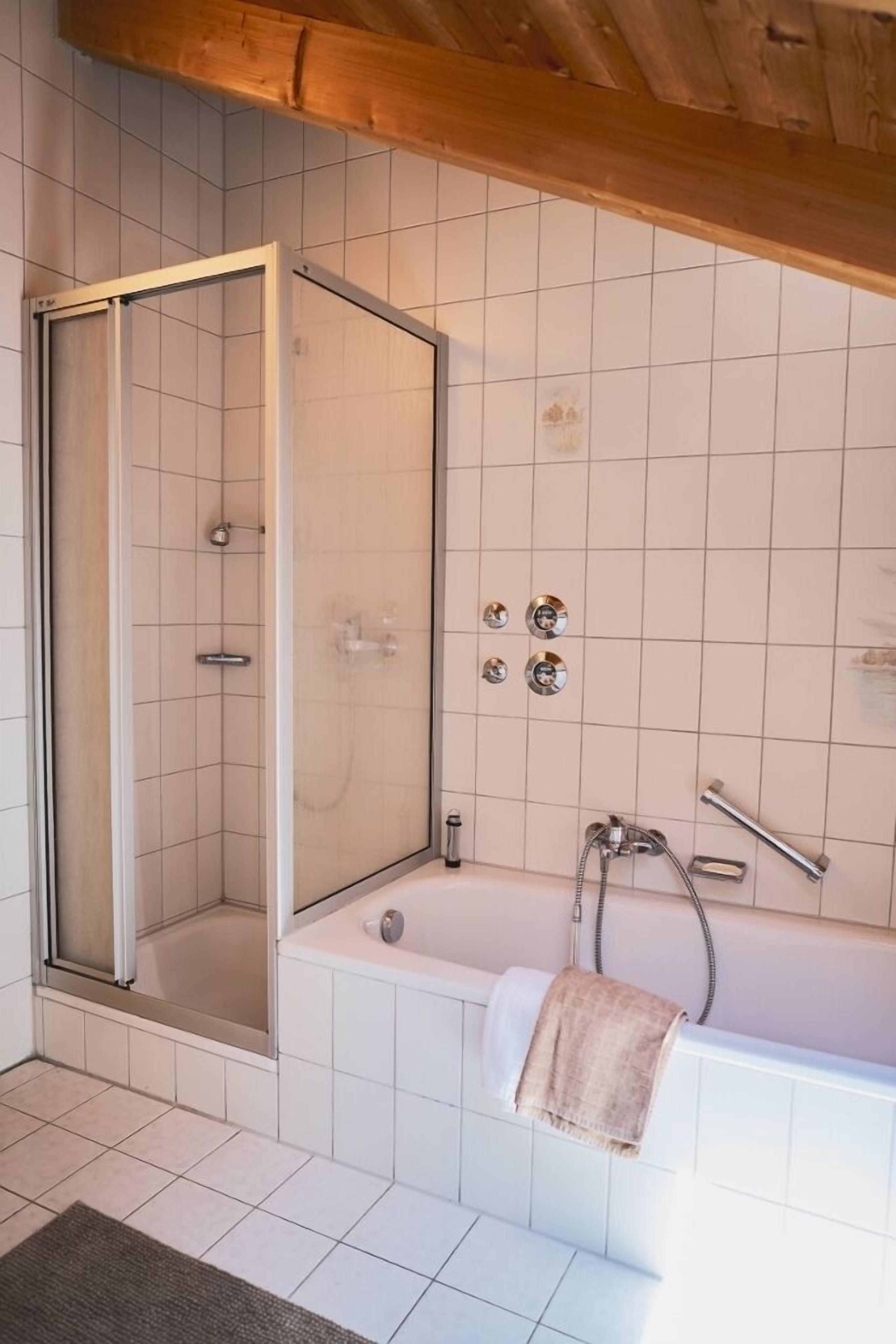 Moderni kylpyhuone, jossa on lasiseinällä varustettu suihku, erillinen kylpyamme ja pyyhekoukku.