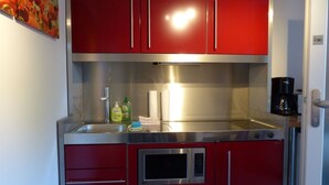 Una cocina compacta con armarios rojos, un lavamanos de acero inoxidable y un microondas.
