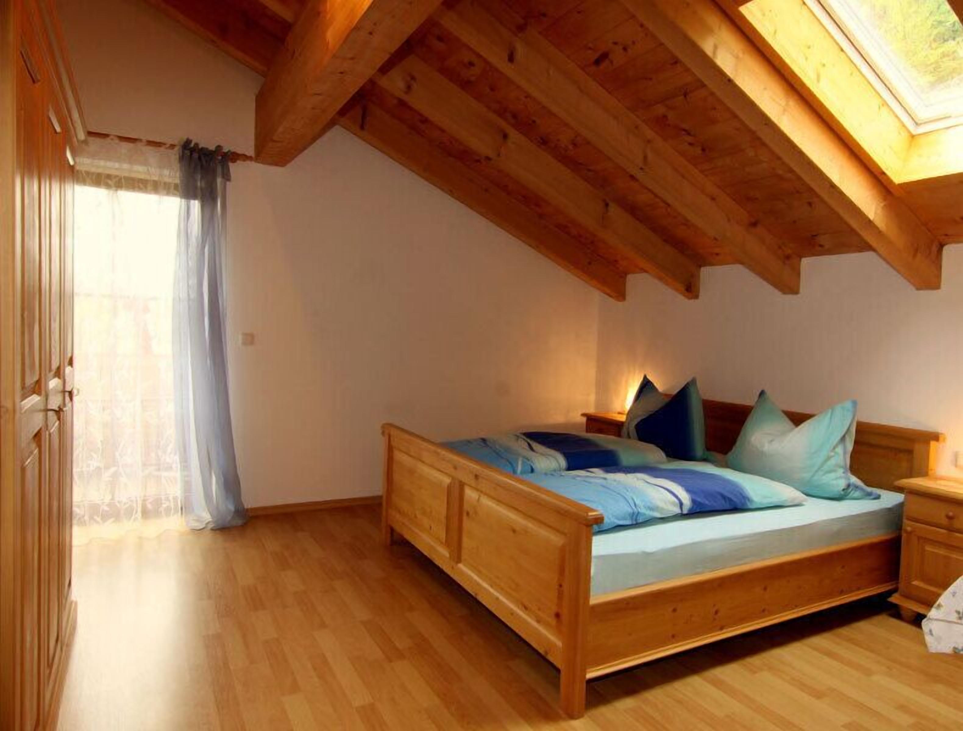 Ein hölzernes Bett in einem Zimmer mit schrägem Dach und Dachfenster.
