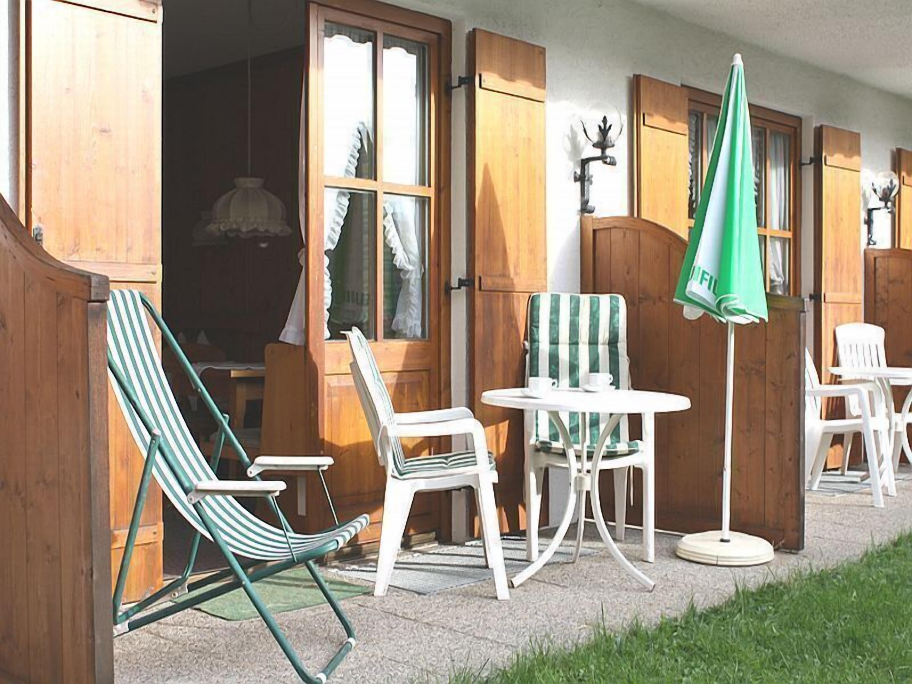 An outdoor seating area with a table and chairs, a green umbrella, and wooden shutters.