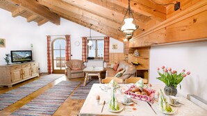 Un comedor acogedor con una mesa de madera dispuesta para una comida, un televisor al fondo y una ventana con cortinas.