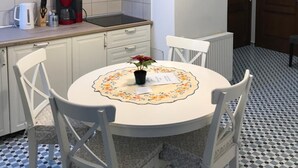 A compact kitchen with white cabinets, a white dining table with chairs, and a hanging light fixture. - House 54 (Brasov)
