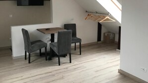 A modern loft with a sloped ceiling, a dining area with a table and chairs, a TV mounted on the wall, and a skylight. - House 54 (Brasov)