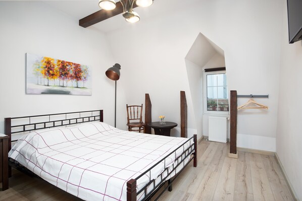 A bedroom with a bed, a painting, a desk, a chair, a table, a hanging light fixture, and a window. - House 54 (Brasov)