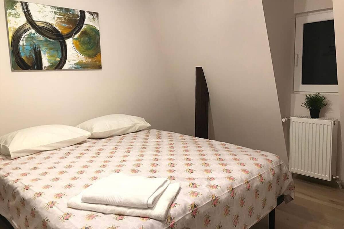 Ein Schlafzimmer mit Bett, Kissen, Heizkörper, Fenster und einem Bild an der Wand.