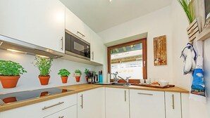 Une cuisine moderne avec des meubles blancs, un four à micro-ondes, un évier et plusieurs plantes en pot.