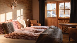 A room with a bed, a chair, a desk, and a window with a view of buildings. - (4) Ferienwohnung 28 qm, Dusche/WC, Kochnische und Balkon (Reit im Winkl)