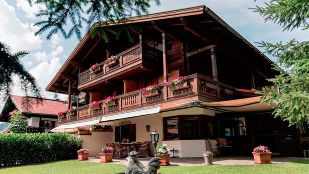 A wooden chalet with a balcony adorned with flowers, a lawn, and outdoor furniture. - (4) Ferienwohnung 28 qm, Dusche/WC, Kochnische und Balkon (Reit im Winkl)