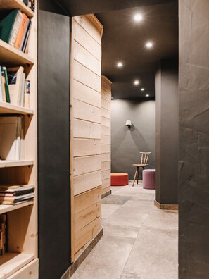 A hallway with a wooden bookshelf, a red ottoman, and a small table with a chair. - (4) Ferienwohnung 28 qm, Dusche/WC, Kochnische und Balkon (Reit im Winkl)