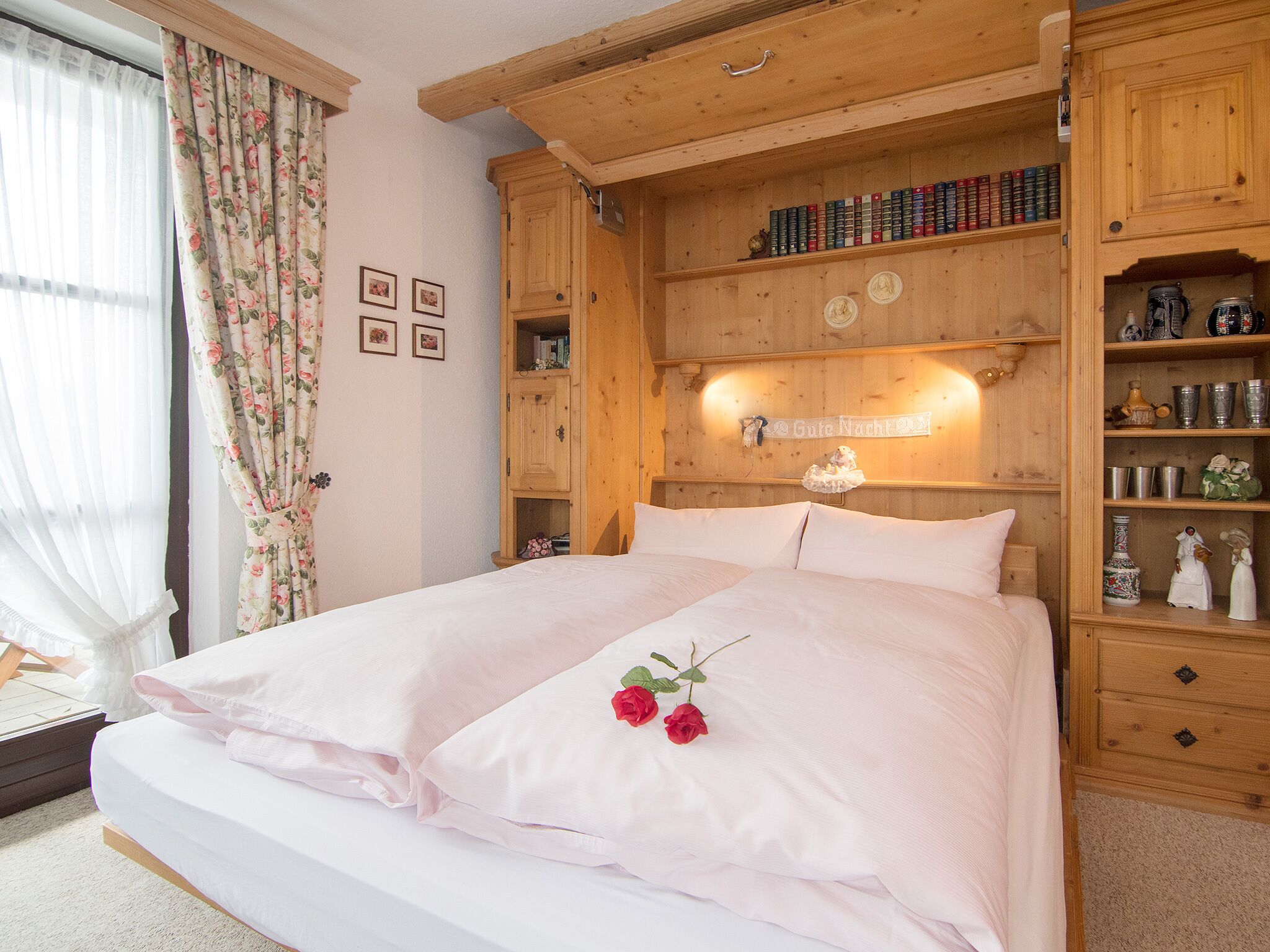 Une chambre à coucher avec une tête de lit en bois, un lit recouvert de linge de maison blanc et une étagère ornée de livres et d’objets décoratifs.