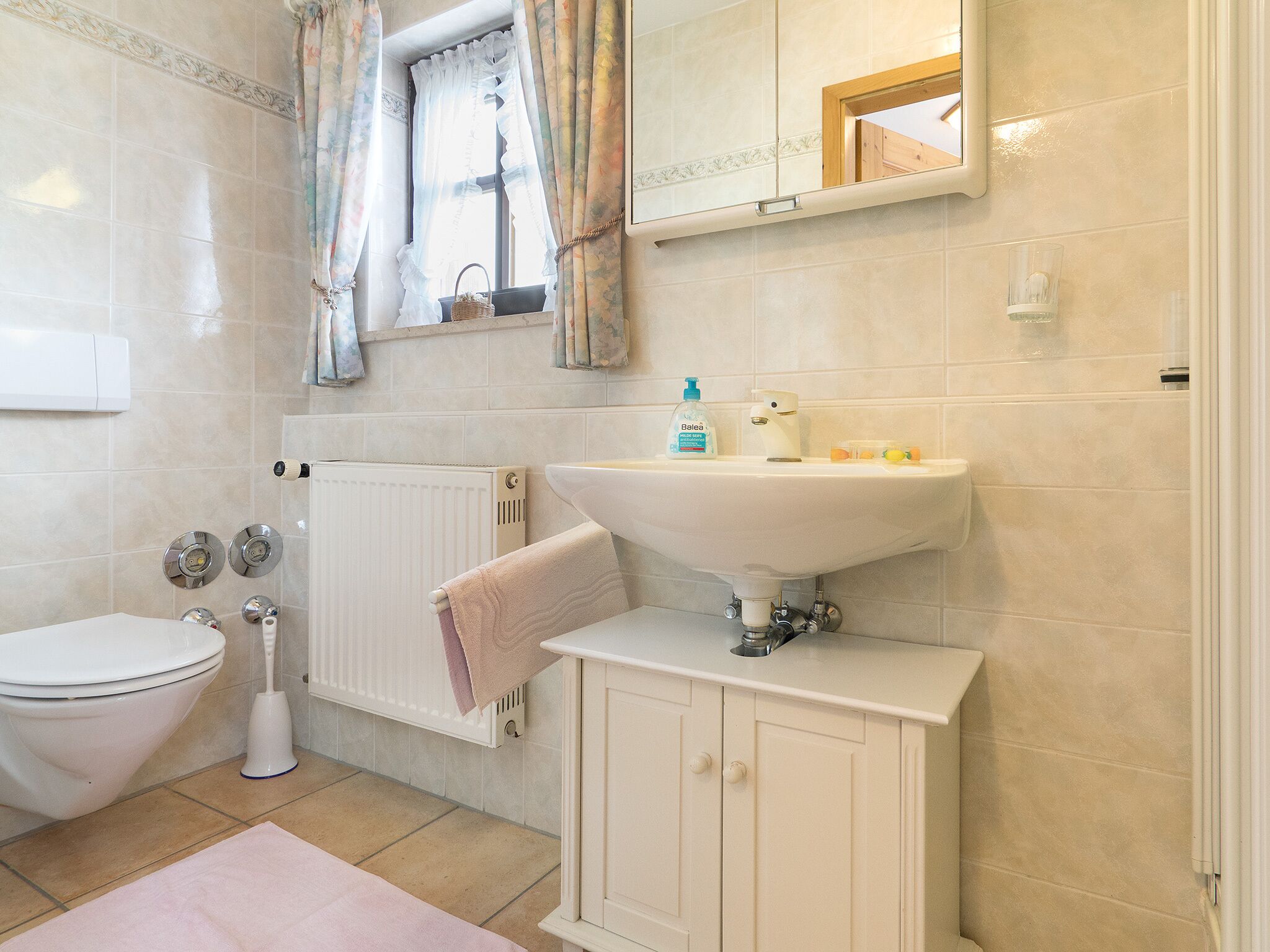 Een badkamer met een toilet, een wastafel, een spiegel en een raam met gordijnen.