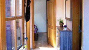 Um corredor com portas de madeira, uma pequena mesa com uma planta e uma cama ao fundo.