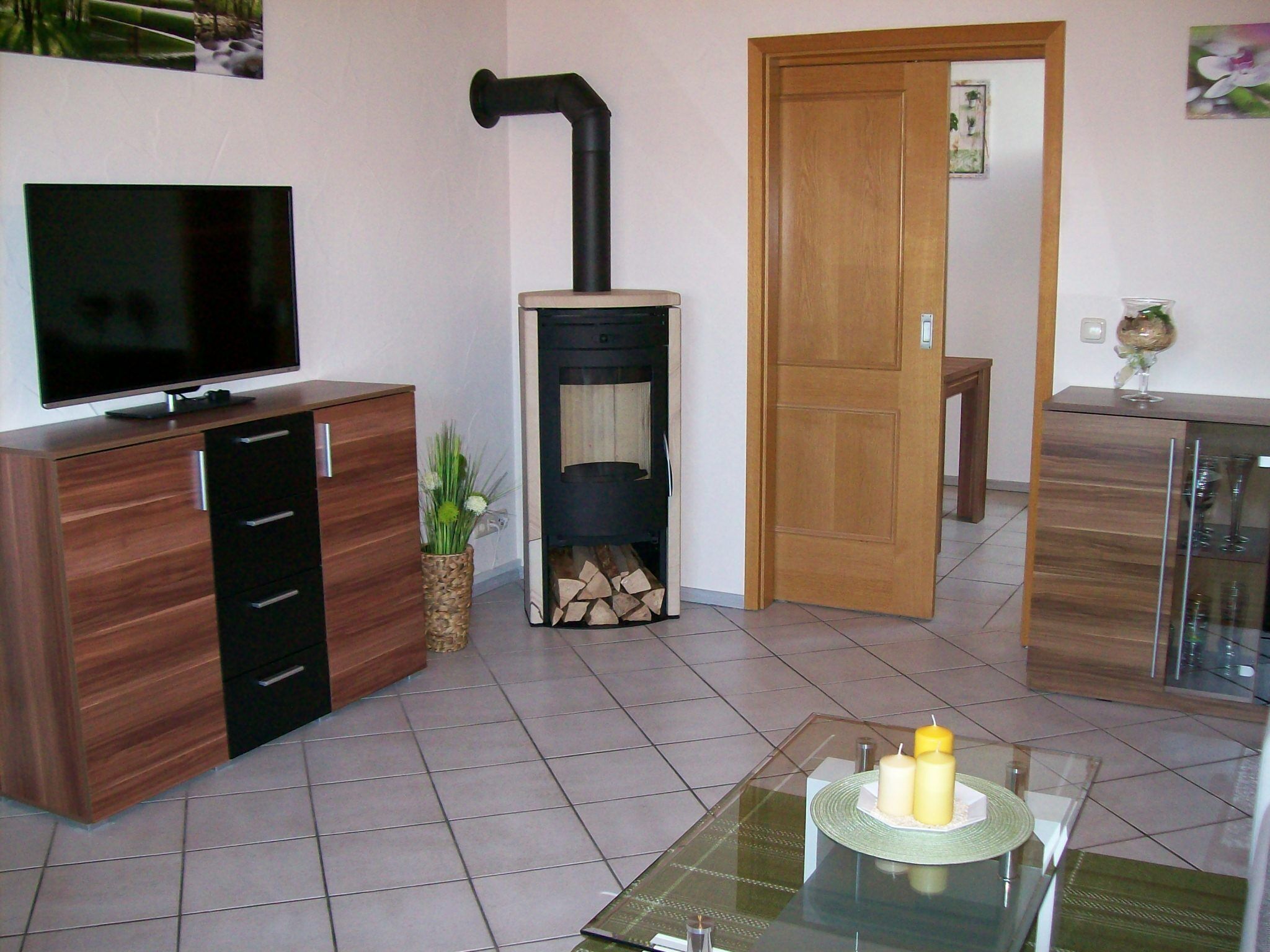 Un soggiorno con una TV su un mobile in legno, un camino, un tavolino da caffè in vetro con candele e una porta che dà su un'altra stanza.