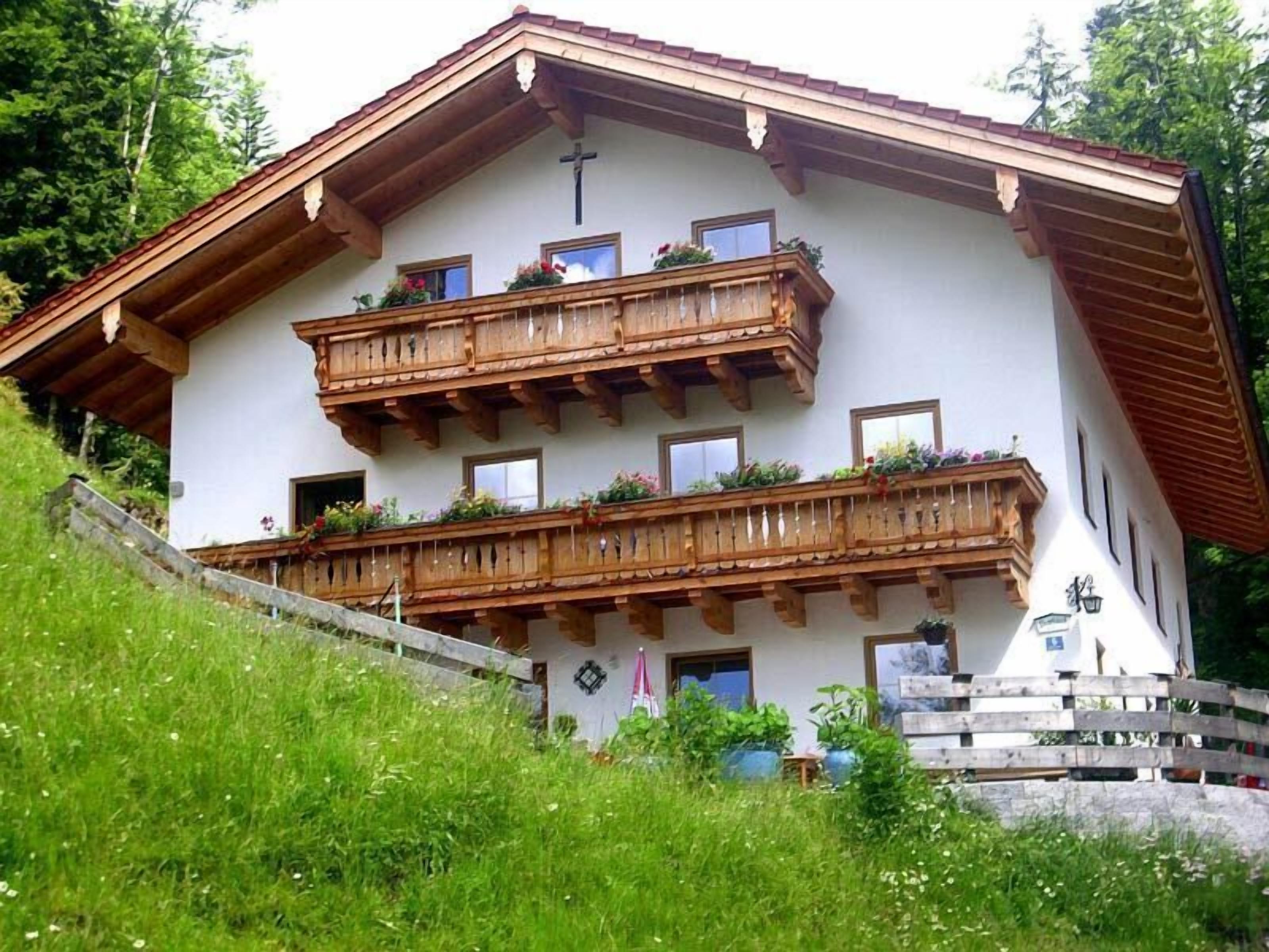 A traditional chalet with wooden balconies, a sloped roof, and a cross above the entrance.