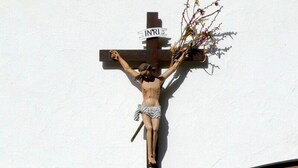 Una cruz de madera fijada en una pared con un cartel encima.