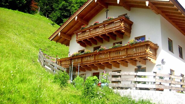 Un chalet de dos pisos con balcones de madera, techo inclinado y fachada blanca.