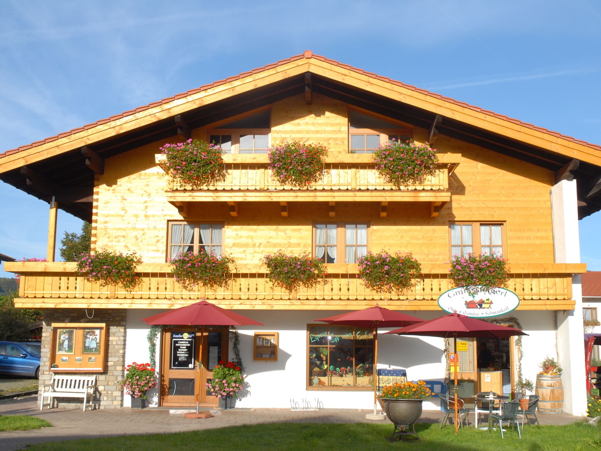 Un bâtiment traditionnel en bois, doté de balcons ornés de fleurs, d’une terrasse et d’une enseigne indiquant qu’il s’agit d’un café.