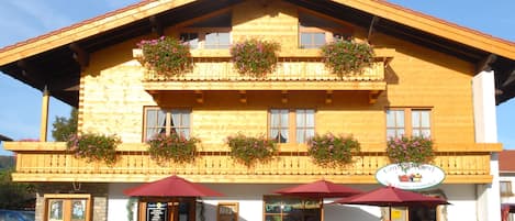 En traditionell byggnad i trä med balkonger som är dekorerade med blommor, utomhusplatser och en skylt som visar att det är ett café.