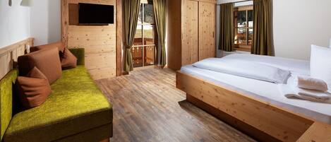 A room with a bed, a sofa, wooden walls, a television, and curtains.