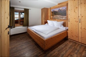 A wooden-framed bedroom with a bed, a radiator, and a window with curtains.