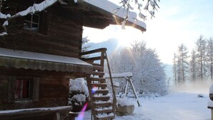 Una baita di legno con l'esterno imbiancato dalla neve, una scala in legno e una panchina all'esterno.