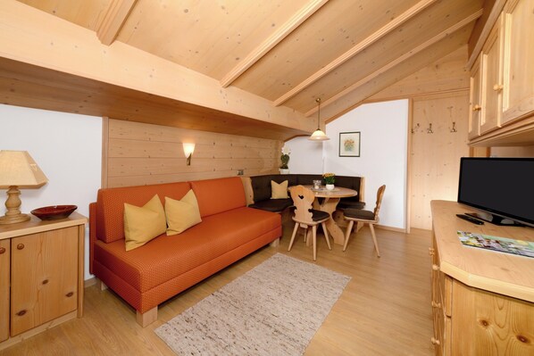 A cozy room with a wooden ceiling, a sofa, a dining table with chairs, a TV, and wooden cabinets.