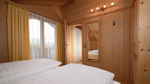 A wooden cabin-style room with two beds, a large window with curtains, and a wooden wardrobe.