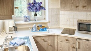 A kitchen with wooden cabinets, a stainless steel sink, a microwave, and a window with a vase of flowers. - Stylish apartment with beautiful mountain scenery (St5)/Steilhofweg. 65 sqm, south-facing balcony (Bayerisch Gmain)