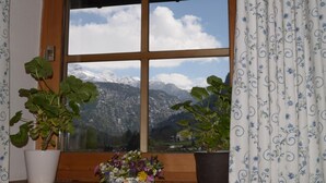 A window with a view of snow-capped mountains, two potted plants on the windowsill, and a floral arrangement. - Alpenhof Punzenlehen (Schoenau am Koenigssee)