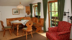 A cozy room with a wooden dining table, chairs, a red floral sofa, and a large window with curtains. - Alpenhof Punzenlehen (Schoenau am Koenigssee)